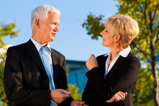 Business people - mature or senior - standing in a park outdoors talking