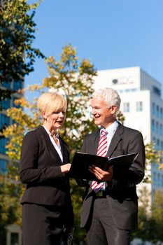 Business people - mature or senior - talking outdoors and discussing a document