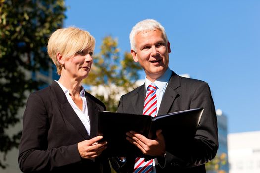 Business people - mature or senior - talking outdoors and discussing a document