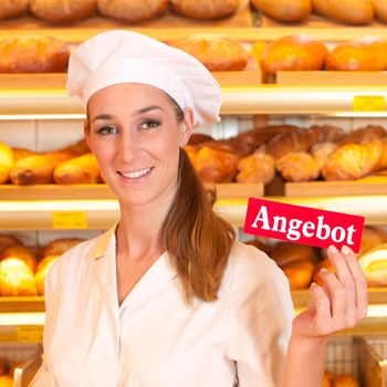 Female baker or saleswoman in her bakery selling fresh bread, pastries and bakery products, she hold a sign in her hand saying "offer" in German
