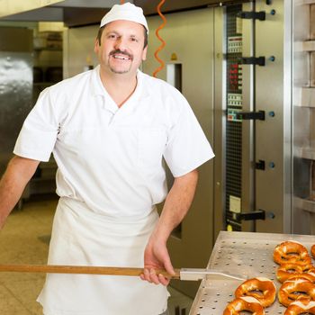 baker standing in his bakery in the morning and is baking bread or buns