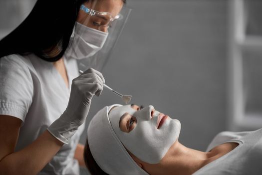 Side view of young beautiful woman lying on procedure for cleaning face in beautician in protective mask. Concept of special beauty procedure for improvements skin face and body.
