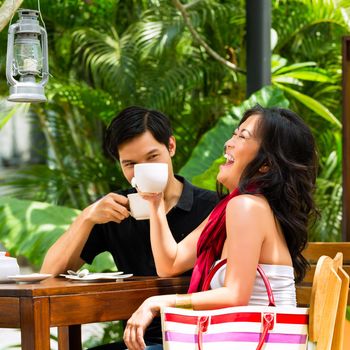 Asian man and woman in restaurant or cafe having fun drinking hot beverage