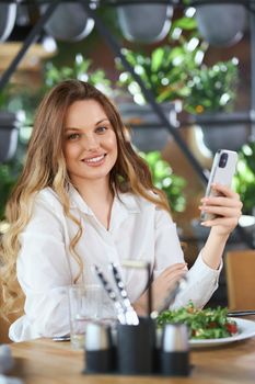 Close up portrait of attractive woman with beautiful smile eating salad in cafe and chatting with friends on phone. Concept of free time or lunch in good mood and tasty food.