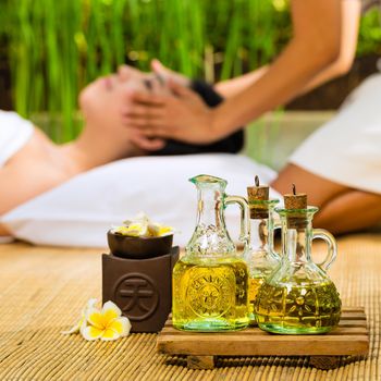 Beautiful Asian woman having a wellness Head massage in a tropical setting and feeling visibly good about it - Essential oils are in the foreground