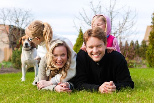 Family, father, mother and daughters, sitting together with their dogs on a meadow, they laugh and have fun