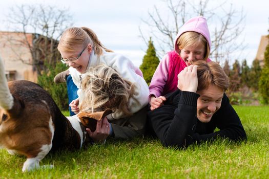 Family, father, mother and daughters, sitting together with their dogs on a meadow, they laugh and have fun