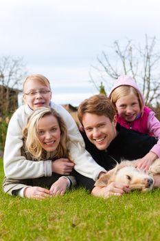 Family, father, mother and daughters, sitting together with their dog on a meadow, they are laughing and have fun