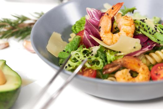 Close up of tasty and juicy pasta with seafood and fresh herbs on white background. Concept of appetizing salad with pasta and avocado,tomatoes at home or restaurant.