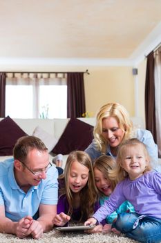 Family - mother, father, daughters - playing with tablet computer lying on the floor at home