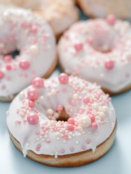 Delicious tender donuts glazed white glaze and sprinkled with pink pearl dressing. Idea decorating donuts for wedding, romantic event, celebration. Selective focus with copy space. Vertical