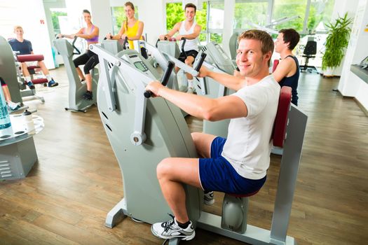 Group of men and women train on machine in a fitness club or gym