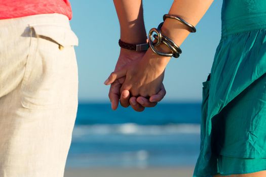 Man and woman, couple, enjoying the romantic sunset on a beach by the ocean in their vacation, they standing hand in hand, closeup