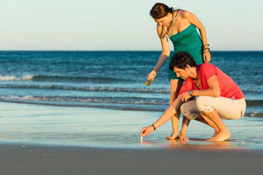 Man and woman, couple, enjoying the romantic sunset on a beach by the ocean in their vacation, they searching shells