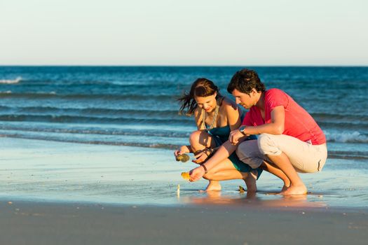 Man and woman, couple, enjoying the romantic sunset on a beach by the ocean in their vacation, they searching shells