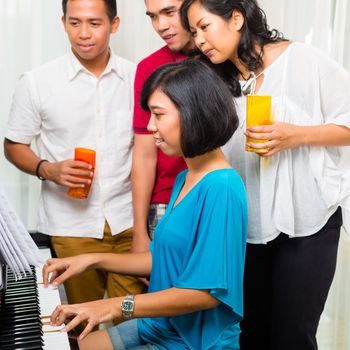 Asian people sitting together at the piano and having fun and smiling