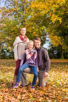 Happy family, Mother, father and daughter or child standing outdoor with colorful leaves and under the trees in autumn or fall