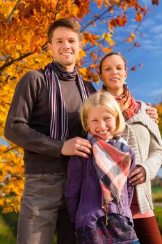 Happy family, Mother, father and daughter or child standing outdoor with colorful leaves and under the trees and blue sky in autumn or fall