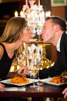 happy couple have a romantic date in a fine dining restaurant they eat spaghetti, a large chandelier is in Background