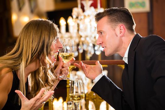 Couple have a quarrel on a romantic date in a fine dining restaurant they are angry and yelling, a large chandelier is in Background