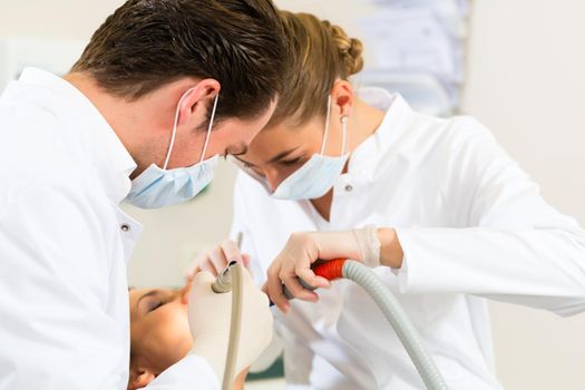 Female patient with dentist and assistant in a dental treatment, wearing masks and gloves