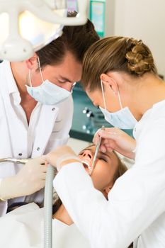 Female patient with dentist and assistant in a dental treatment, wearing masks and gloves