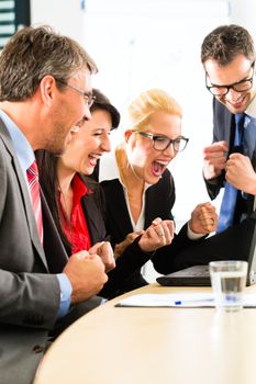 Business - Four professionals in office in business attire looking at laptop screen working together, they rejoice