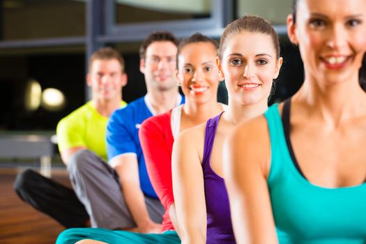 Group of young people stretching in gym for better fitness led by instructor