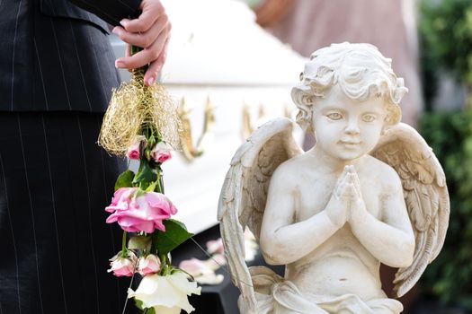 Mourning woman on funeral with pink rose standing at casket or coffin