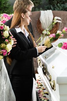 Mourning man and woman on funeral with pink rose standing at casket or coffin