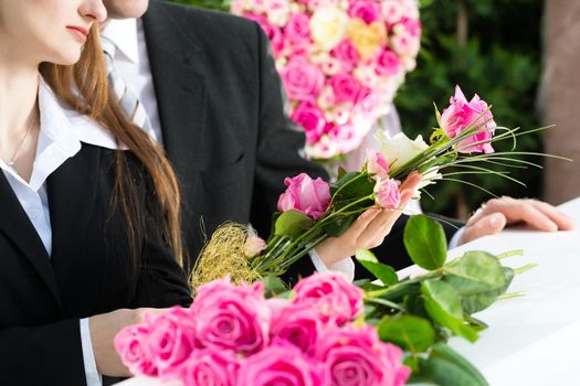 Mourning man and woman on funeral with pink rose standing at casket or coffin