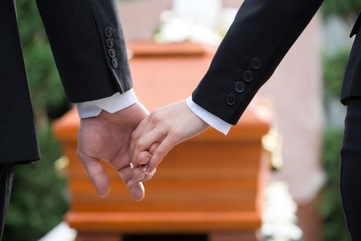 Religion, death and dolor - couple at funeral holding hands consoling each other in view of the loss