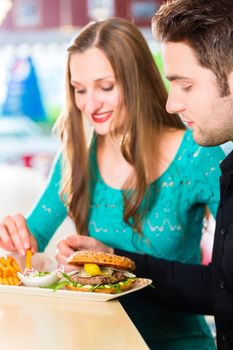 Friends or couple eating fast food with burger and fries in American fast food diner