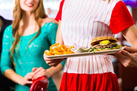 Friends or couple eating fast food in American fast food diner, the waitress wearing a short costume serving a meal