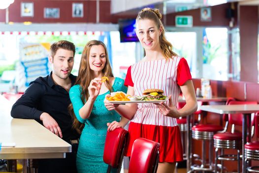 Friends or couple eating fast food in American fast food diner, the waitress wearing a short costume