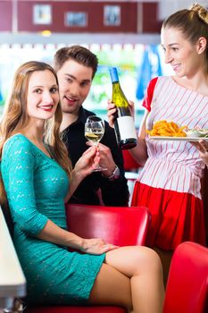 Friends or couple eating fast food in American fast food diner, the waitress serving the food and wine