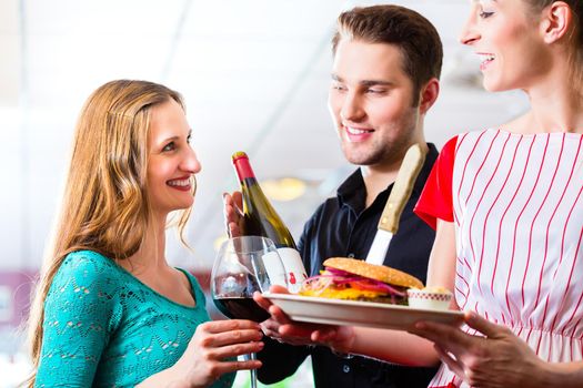 Friends or couple eating fast food in American fast food diner, the waitress serving the food, burgers, fries, and red wine