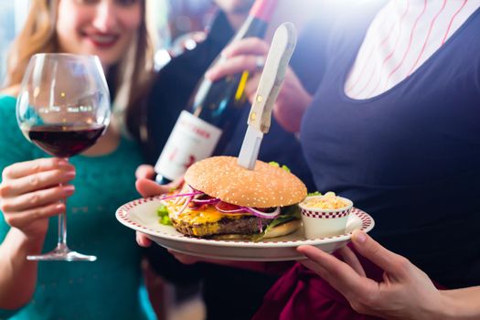 Friends or couple eating fast food in American fast food diner, the waitress serving the food, burgers, fries, and red wine