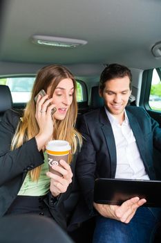 Young businesspeople with mobile phone and tablet computer traveling in taxi, they are colleagues