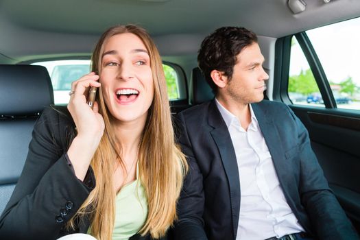 Young businesspeople traveling in taxi, she is busy on the phone, they are colleagues