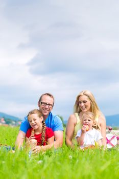 Happy family with daughter or kids sitting in a meadow in summer eating food on picnic