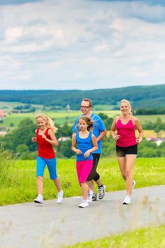 Family - mother, father and four children - doing jogging or outdoor sport for fitness on rural street