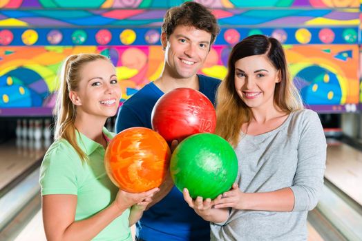 Young people or friends, man and women, playing bowling with a ball in front of the ten pin alley, they are a team