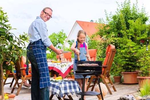 Father and daughter making barbecue in the garden in summer with sausages and meat