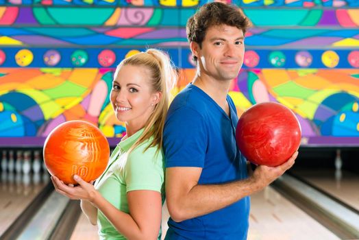 Young couple or friends, man and woman, playing bowling with a ball in front of the ten pin alley, they are a team