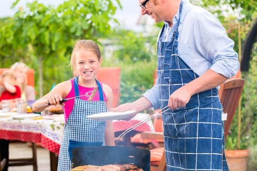 Father and daughter making barbecue in the garden in summer with sausages and meat