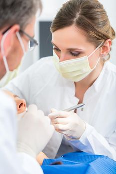 Female patient with dentist and assistant in a dental treatment, wearing masks and gloves