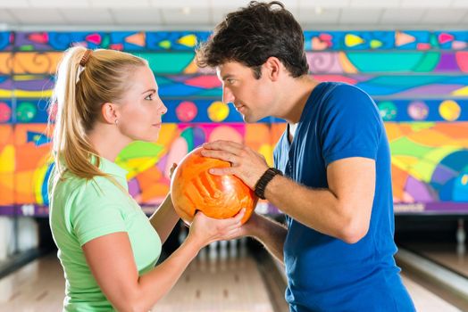 Young couple or friends, man and woman, playing bowling with a ball in front of the ten pin alley, they are a team