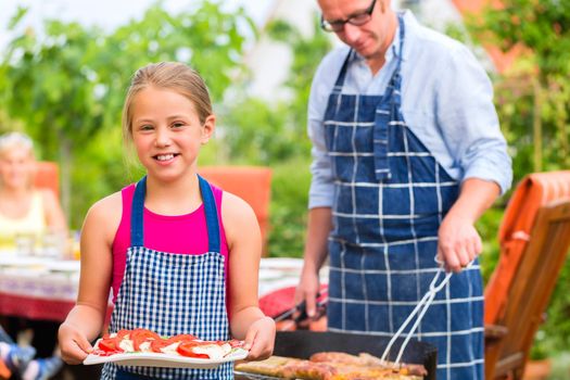 Father and daughter making barbecue in the garden in summer with sausages and meat