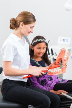 Dentist in surgery holds denture and explains a child patient with a toothbrush